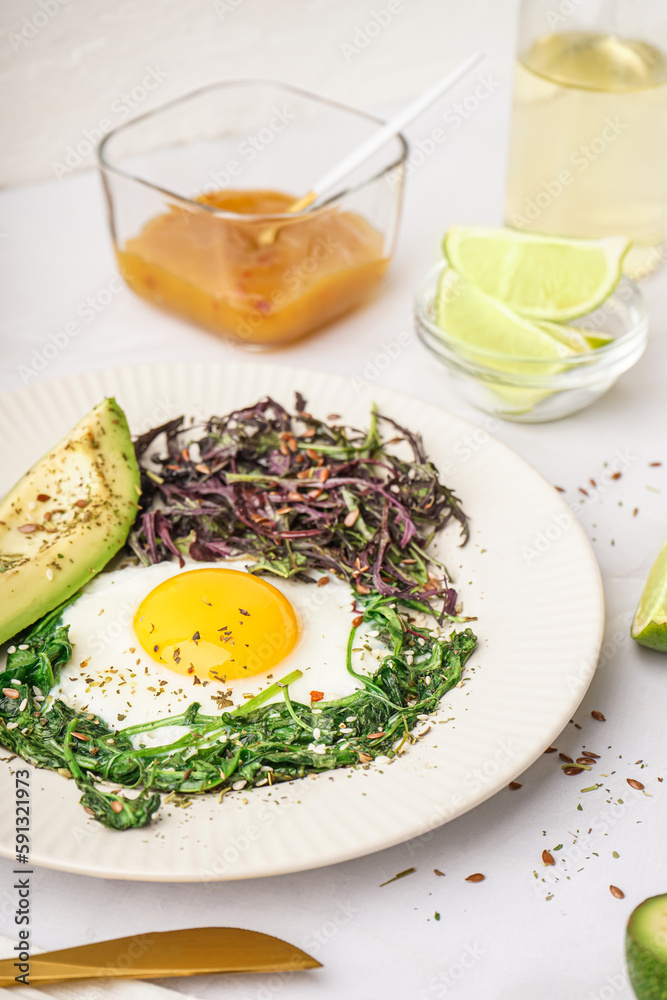 Plate with tasty fried egg, avocado and greens on light background