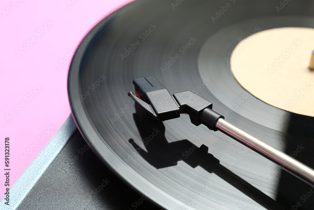 Record player with vinyl disk on pink background, closeup