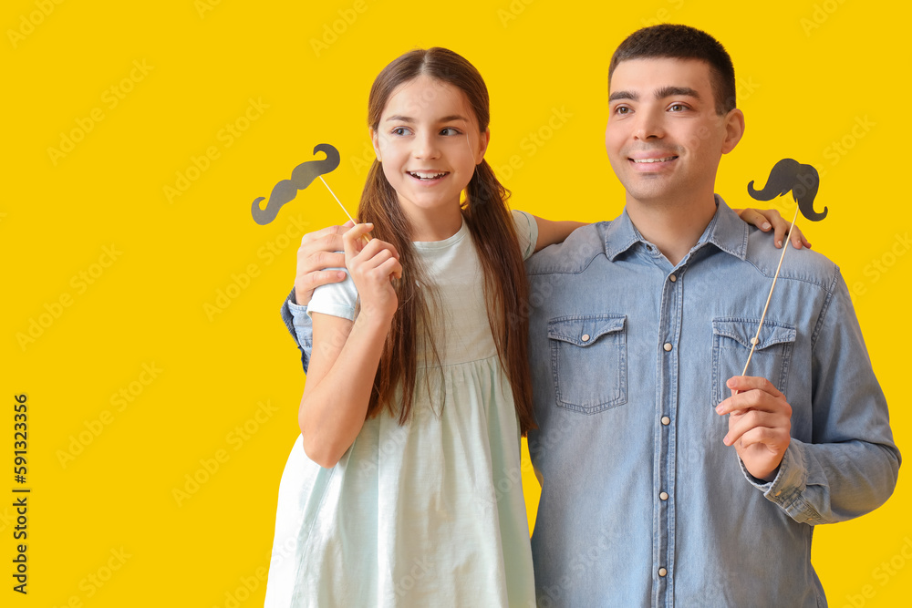 Portrait of father and his little daughter with paper mustache on yellow background