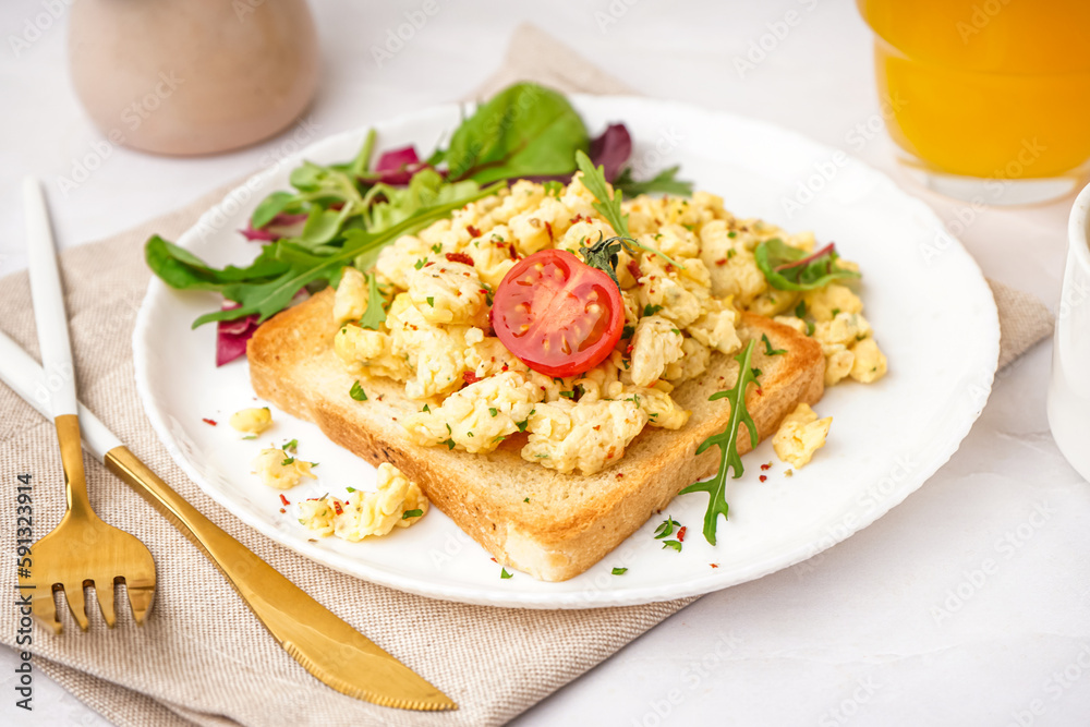 Plate with tasty scrambled eggs sandwich and salad on light background