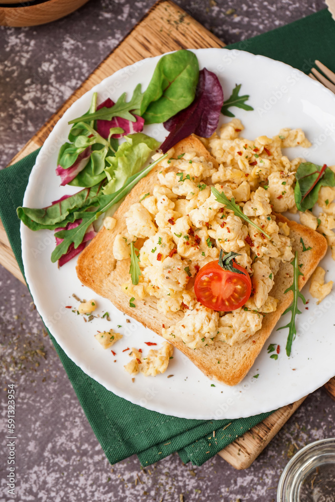 Plate with tasty scrambled eggs sandwich and salad on grey background