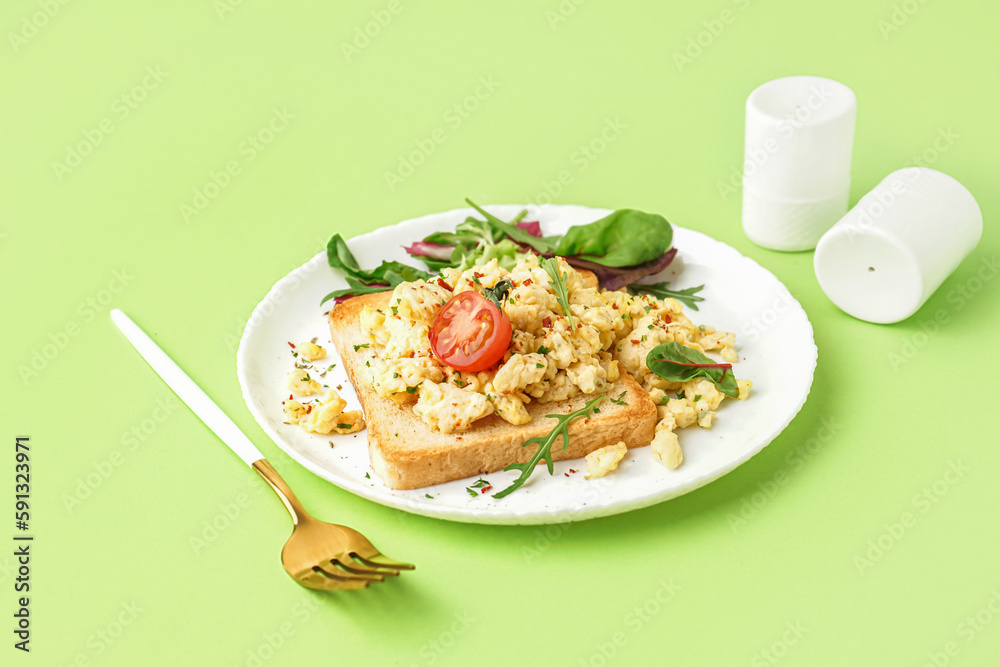 Plate with tasty scrambled eggs sandwich and salad on green background