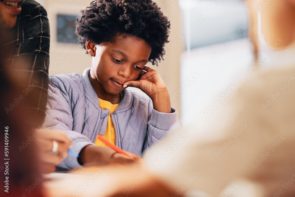 Black kid writing his work in a primary school class