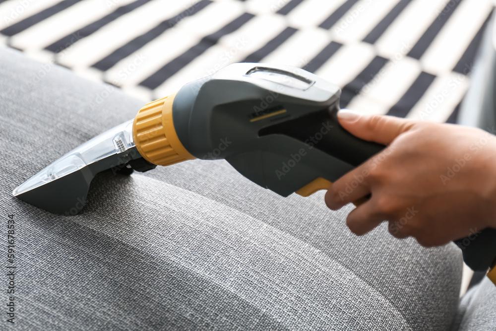 Woman removing dirt from sofa at home, closeup