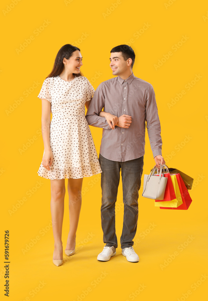 Lovely young couple with shopping bags walking hand in hand on yellow background