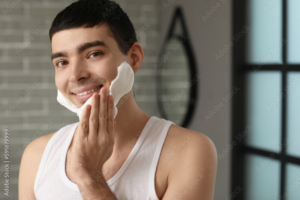 Young man applying shaving foam onto face in bathroom