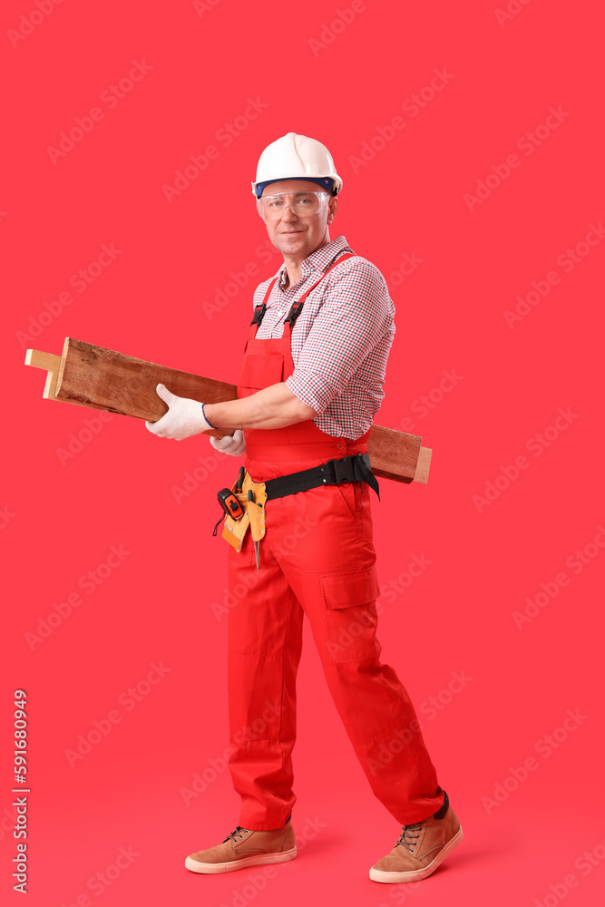 Mature carpenter with wooden planks on red background