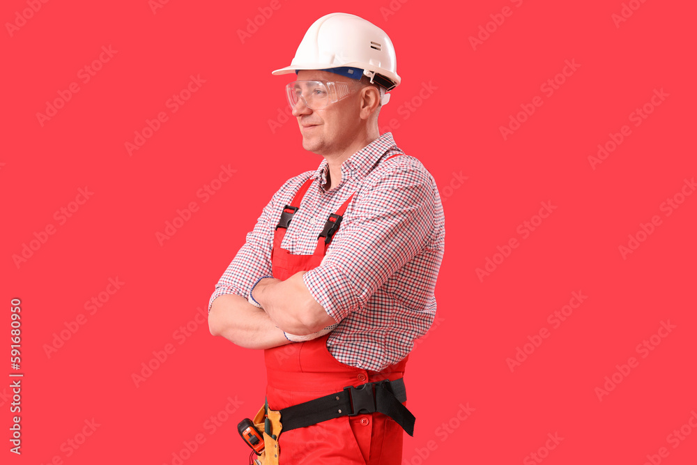 Mature carpenter in hardhat on red background