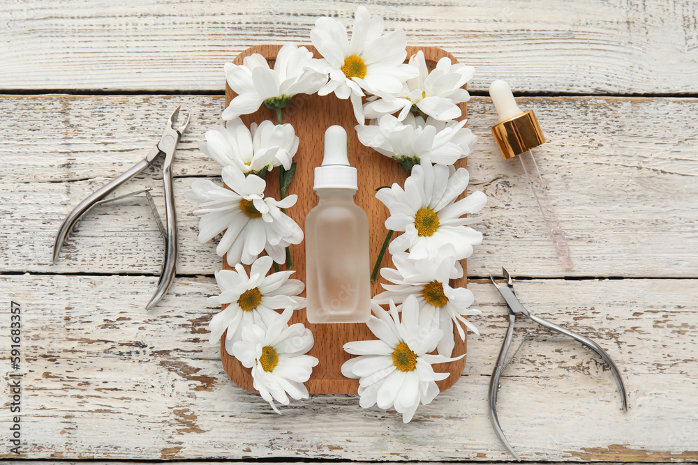 Composition with bottle of cuticle oil, manicure instruments and chamomile flowers on light wooden b