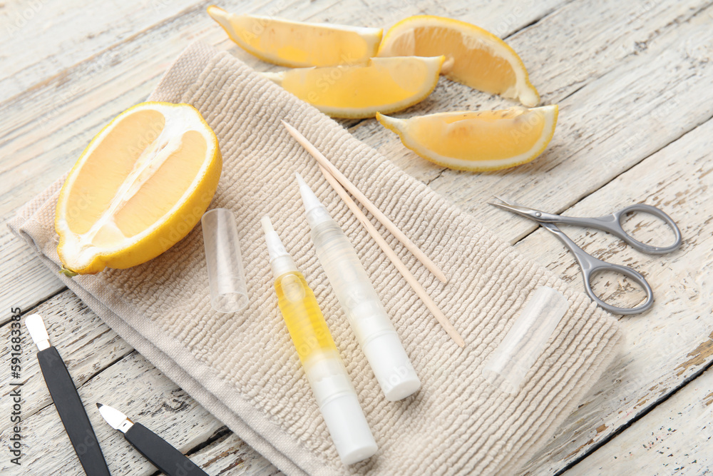 Composition with cuticle oil pens, manicure instruments and lemon on light wooden background, closeu