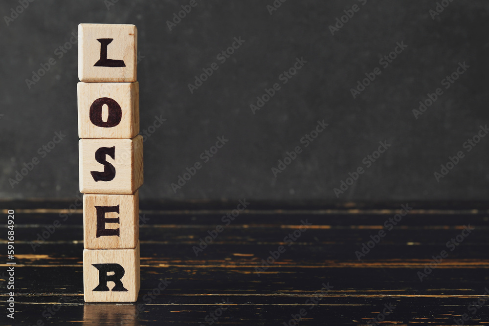 Wooden cubes with word LOSER on table near dark wall