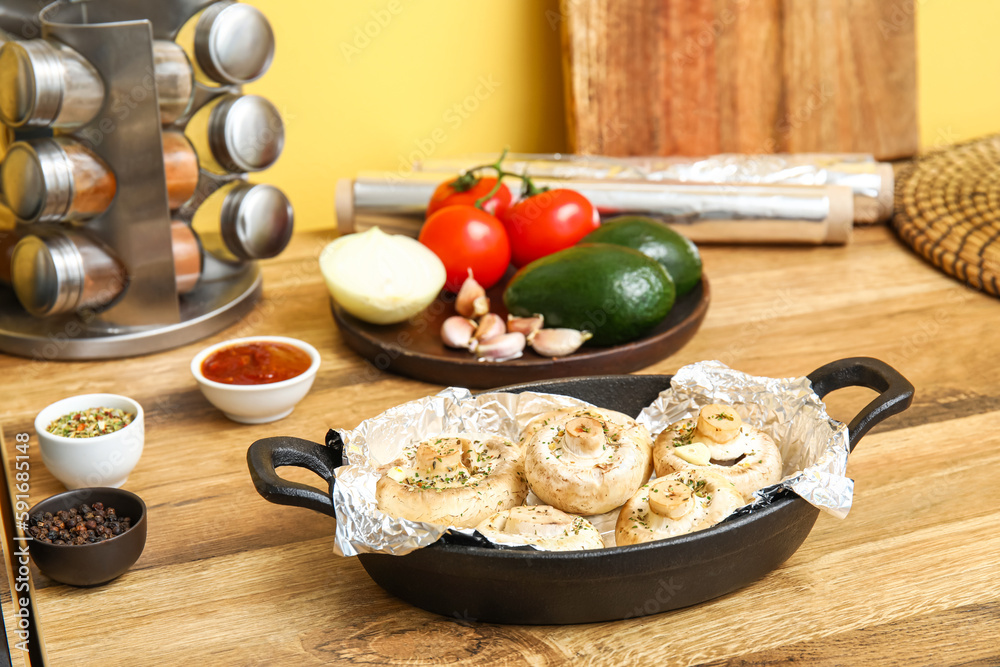 Baking dish with raw mushrooms, spices and vegetables on wooden table in kitchen