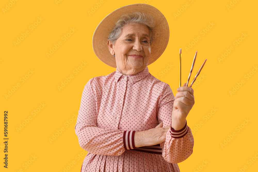 Senior woman with makeup brushes on yellow background