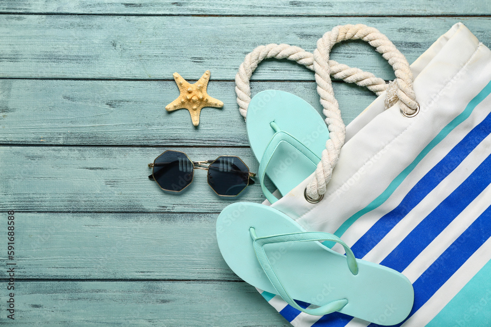 Flip-flops with bag, sunglasses and starfish on blue wooden background