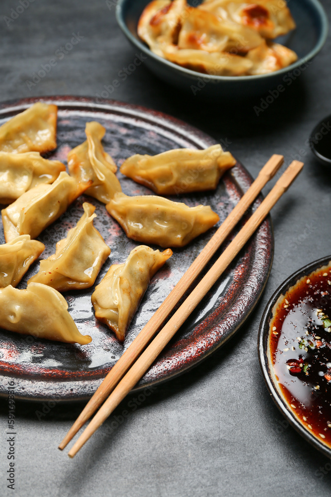 Plate with tasty Chinese jiaozi and sauce on black background