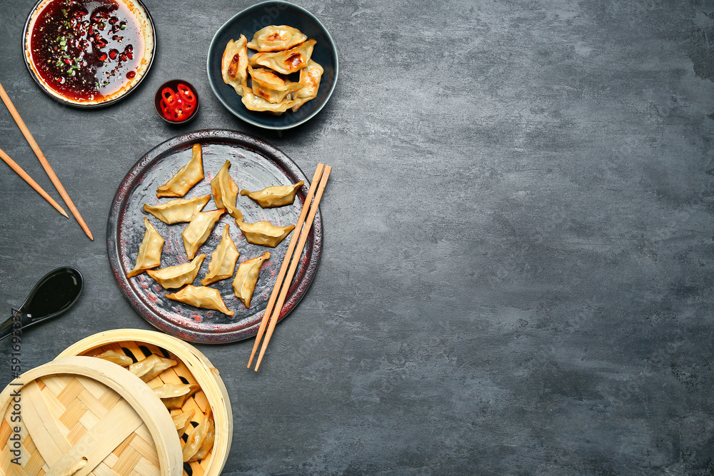 Plate with tasty Chinese jiaozi, bamboo steamer and sauce on black background