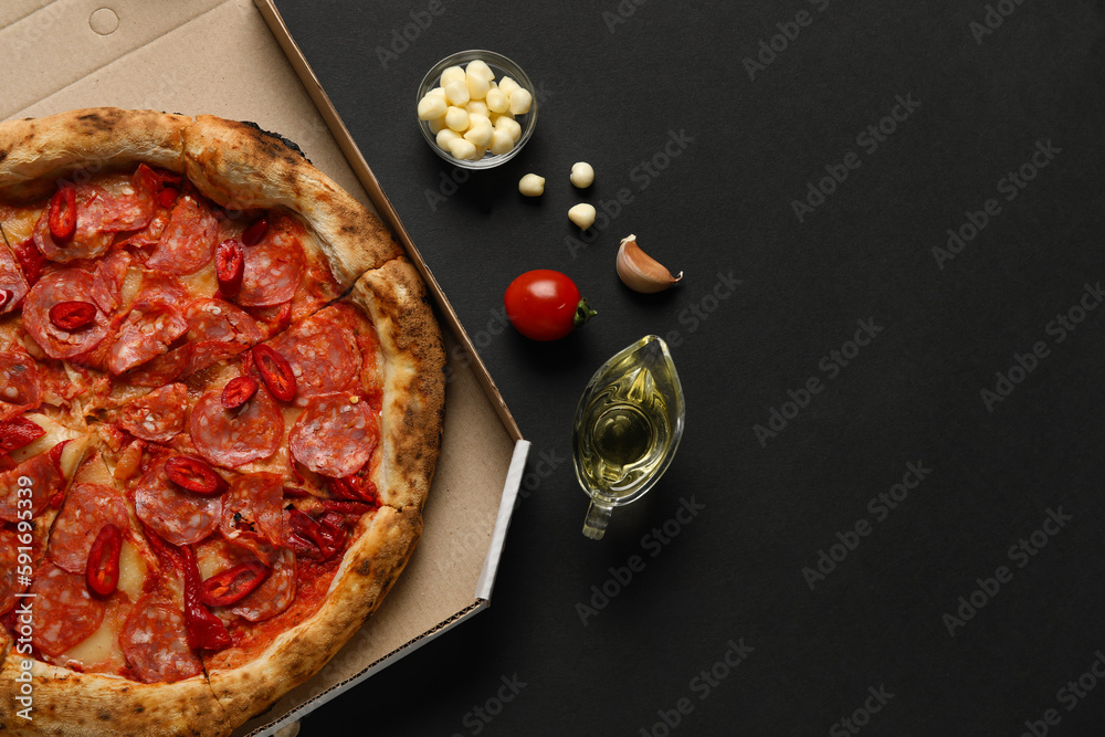 Cardboard box with delicious pepperoni pizza and ingredients on black background