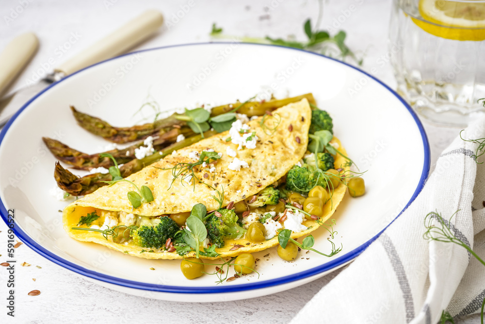 Tasty omelet with broccoli, asparagus and pea on light table