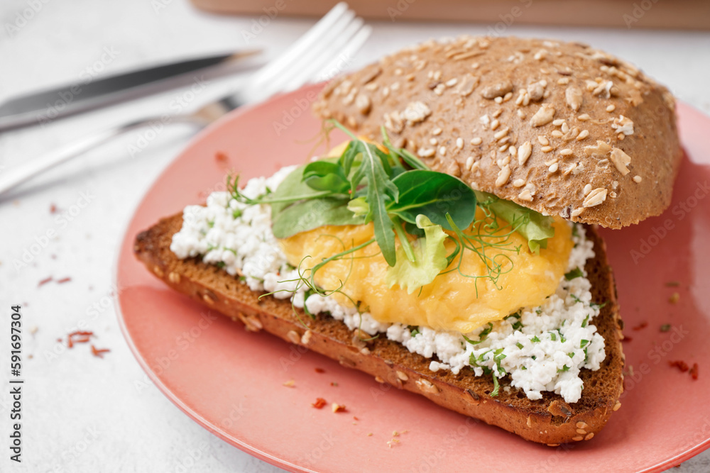 Plate with tasty scrambled eggs sandwich on light background