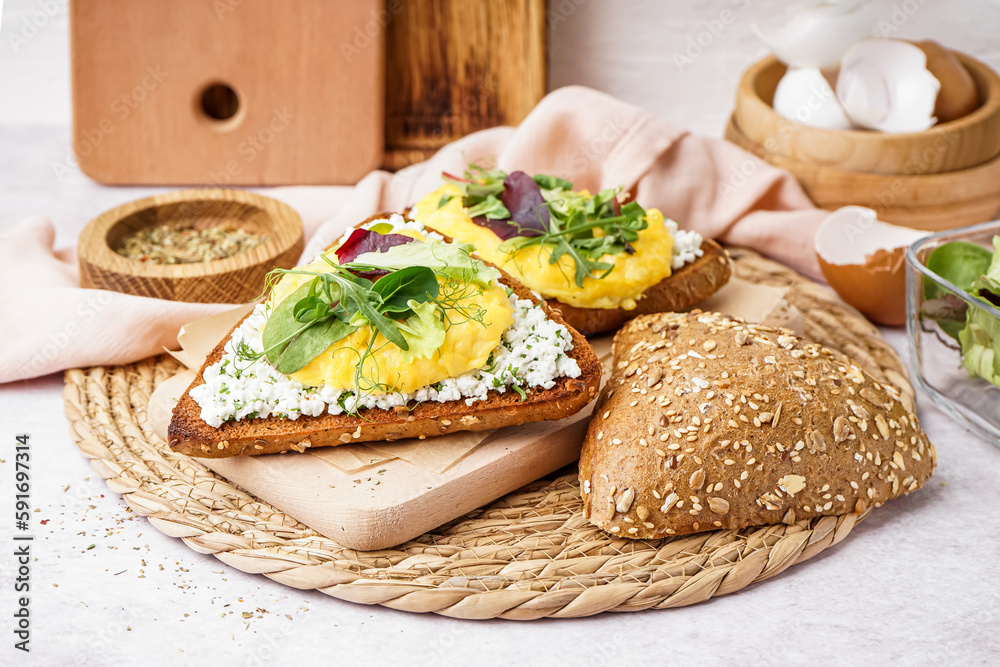 Wooden board with tasty scrambled eggs sandwich on light background