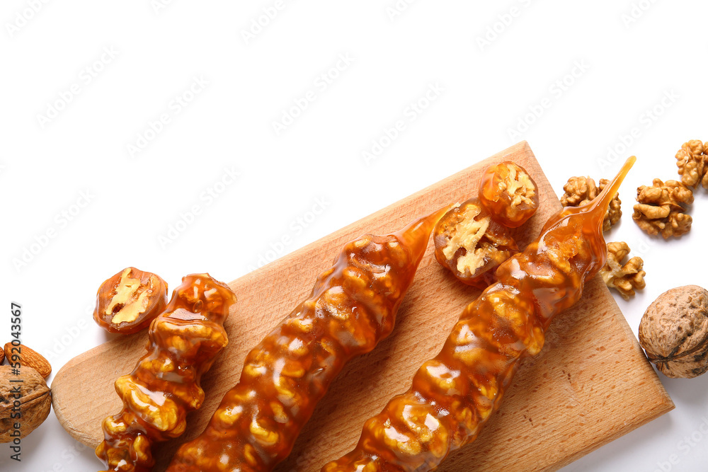 Wooden board with tasty churchkhela and walnuts on white background