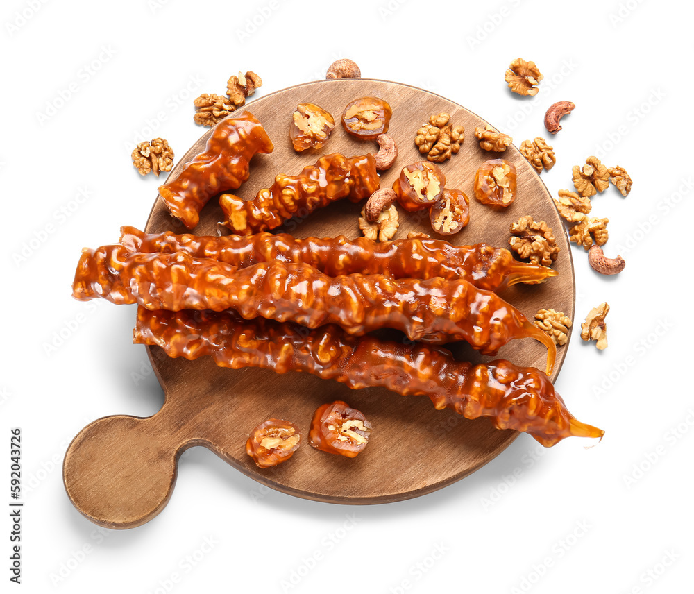 Wooden board with tasty churchkhela and nuts on white background