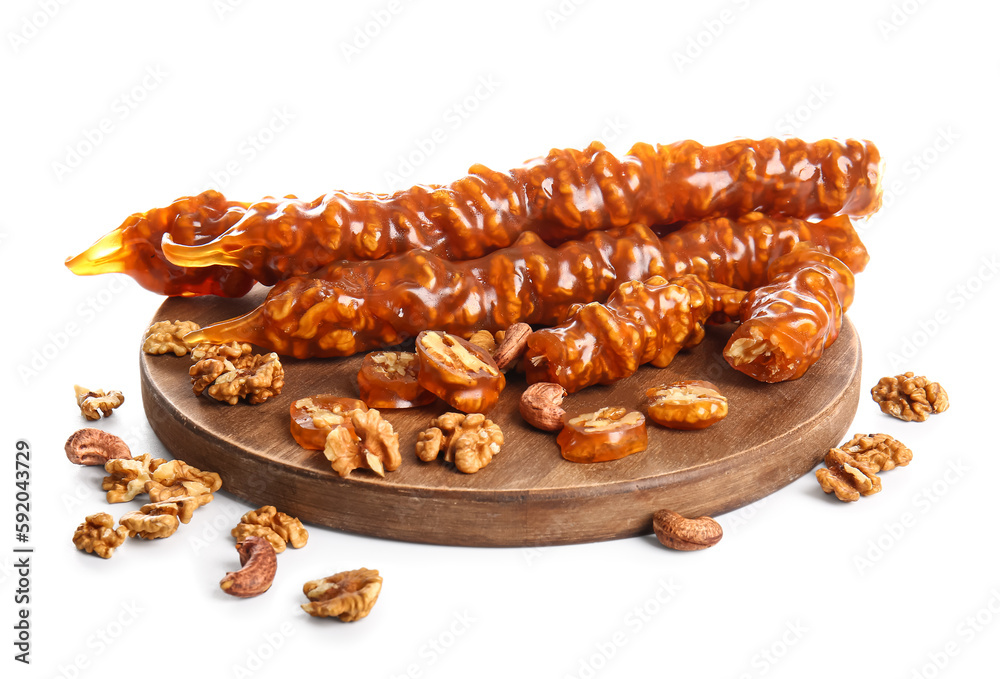 Wooden board with tasty churchkhela and nuts on white background