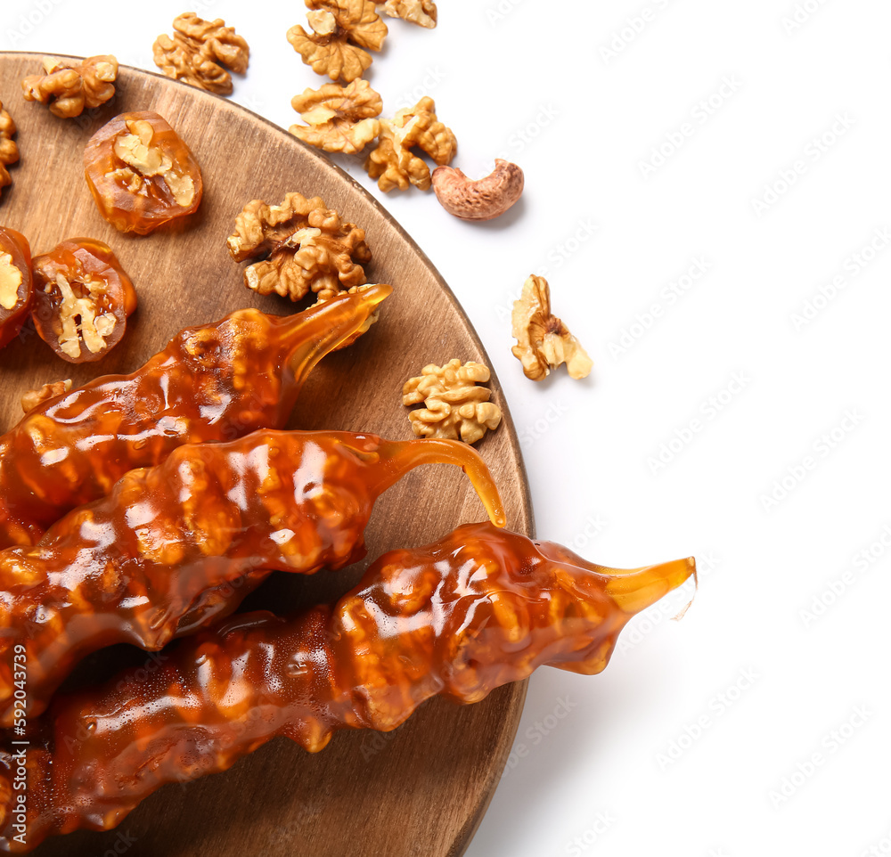 Wooden board with tasty churchkhela and nuts on white background, closeup