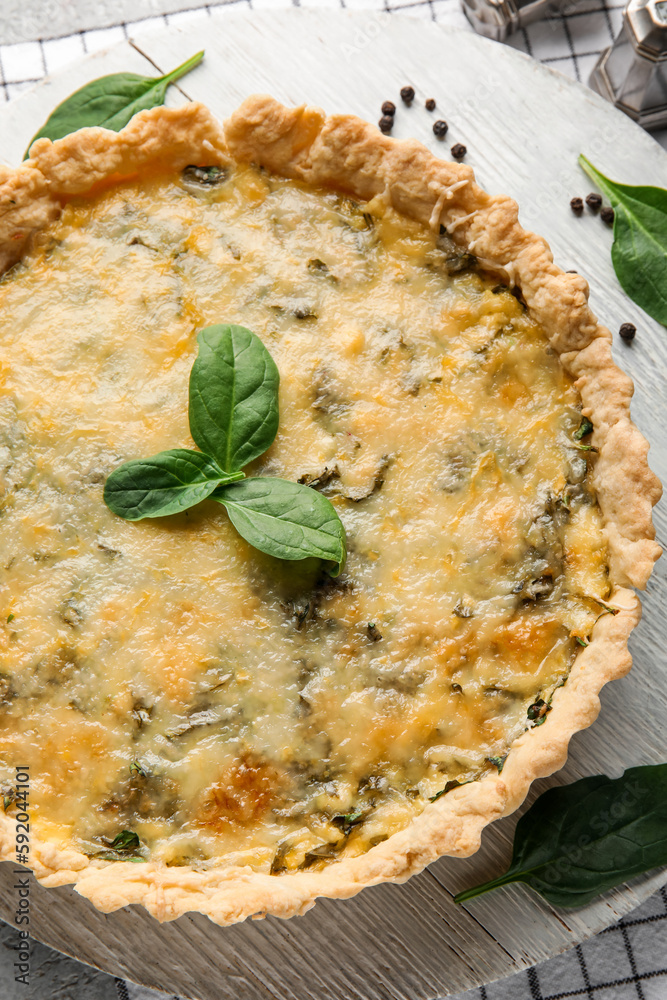 Board with delicious quiche and spinach leaves, closeup