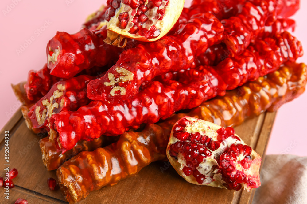 Board with delicious churchkhela and pomegranate on pink background