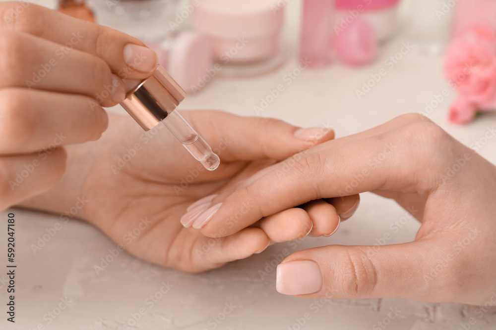 Manicure master applying cuticle oil onto female fingernails on light background, closeup