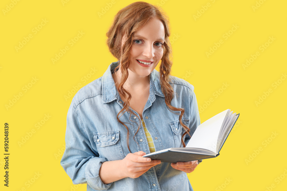 Beautiful redhead woman with book on yellow background