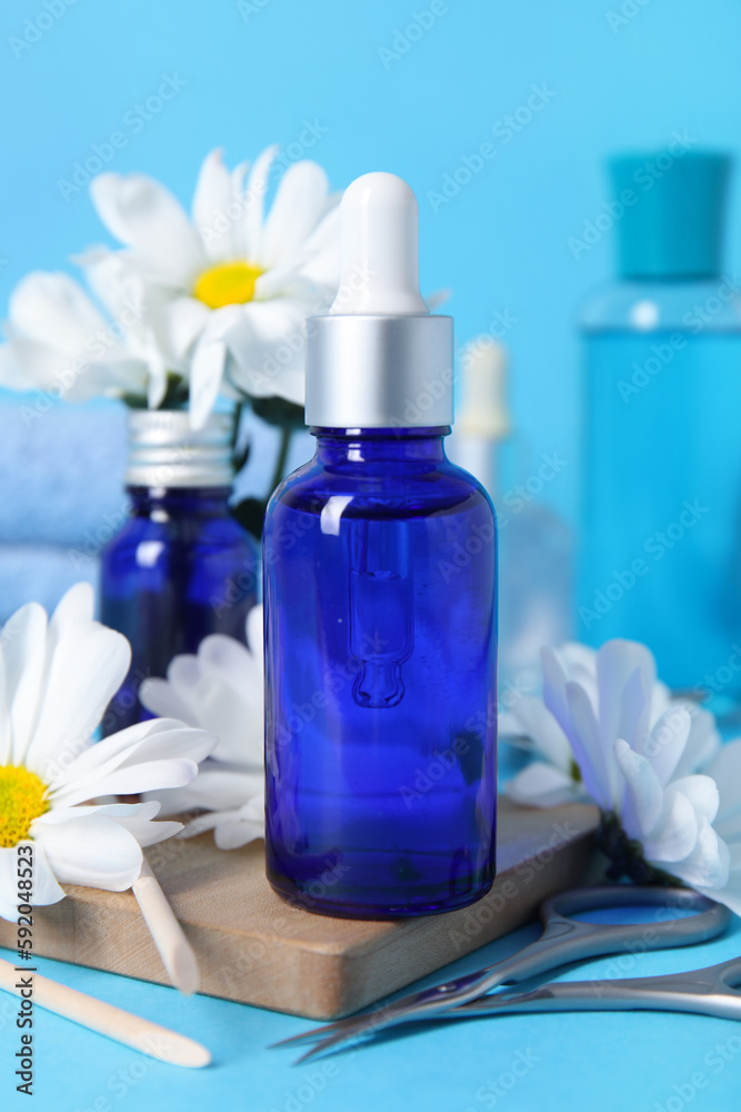 Composition with bottles of cuticle oil, manicure instruments and chamomile flowers on color backgro