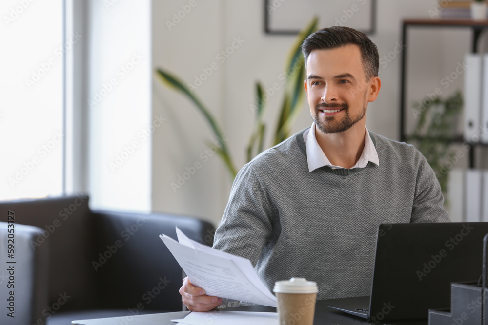 Handsome businessman working with documents at table in office