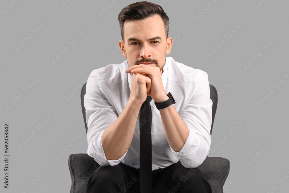 Handsome businessman sitting in armchair on grey background