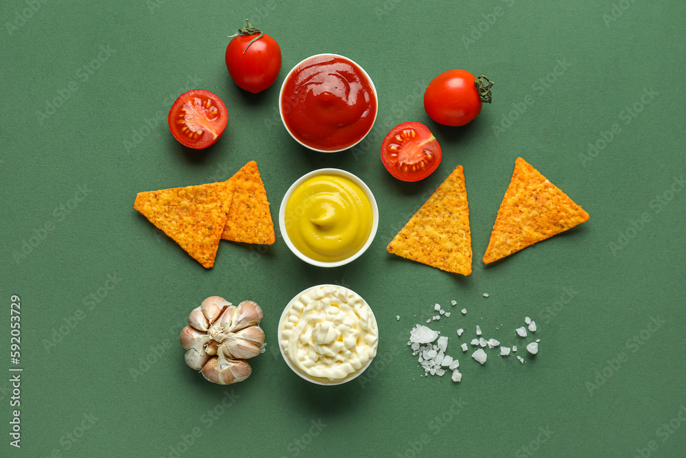 Composition with different sauces, nachos and vegetables on green background