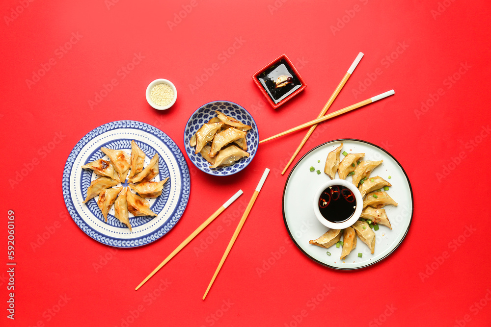 Plates with tasty Chinese jiaozi and sauce on red background