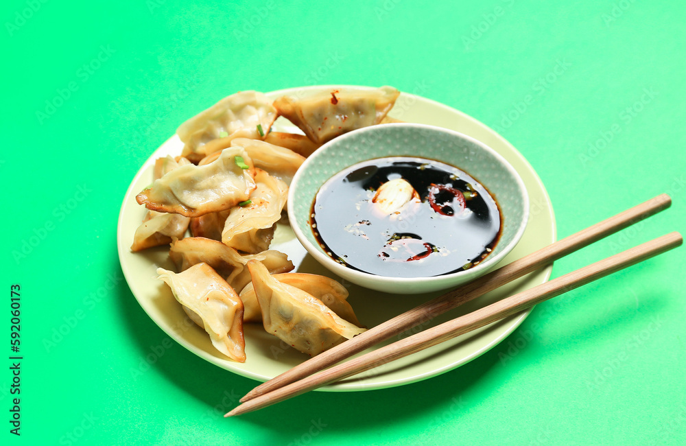 Plate with tasty Chinese jiaozi and sauce on green background