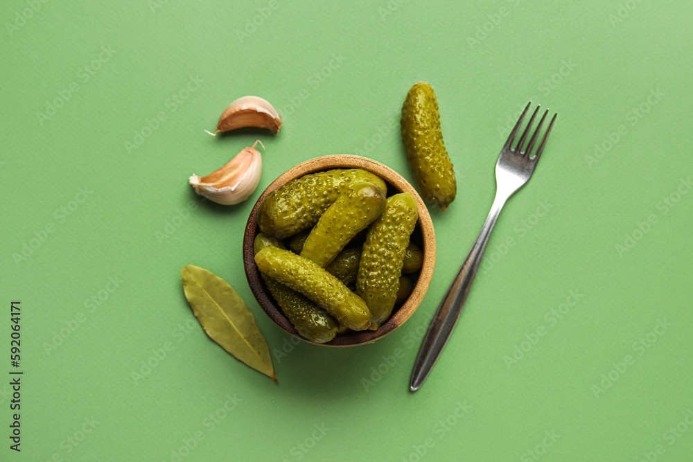 Bowl with tasty fermented cucumbers and ingredients on green background