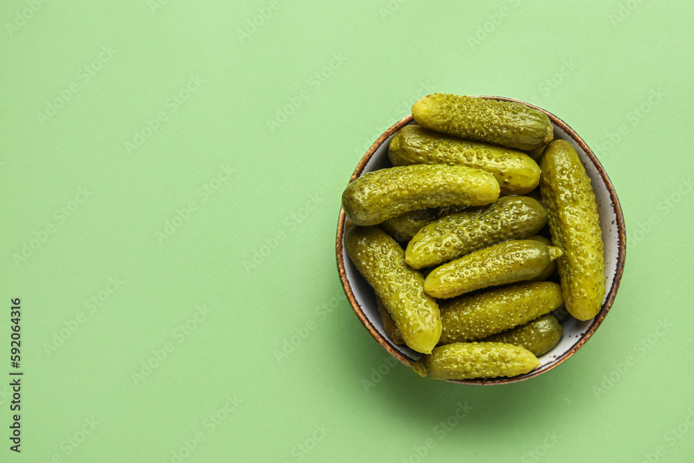 Bowl with tasty fermented cucumbers on green background