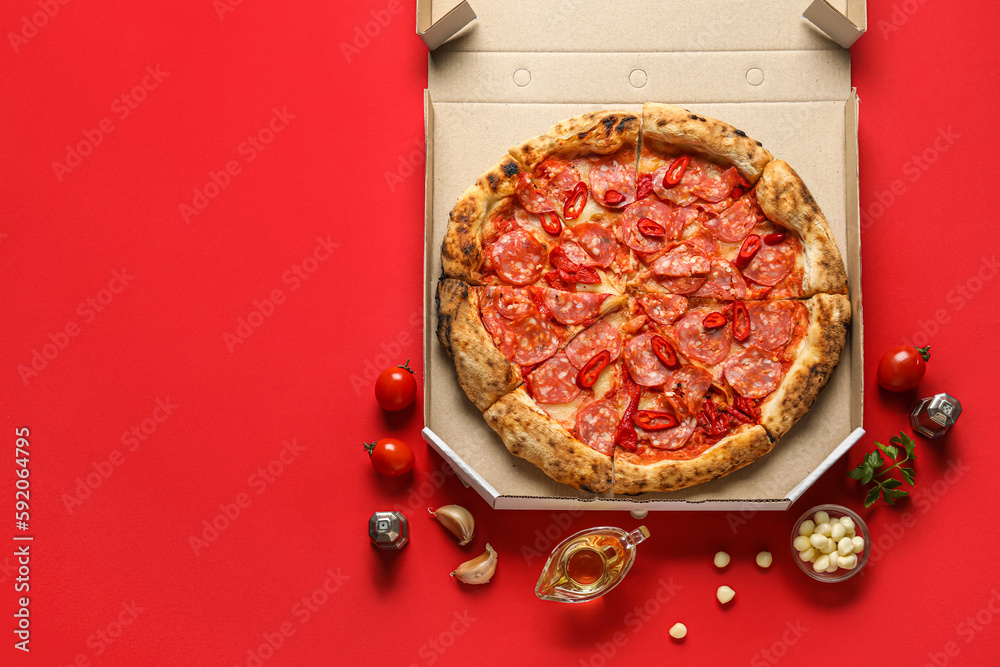 Cardboard box with delicious pepperoni pizza and ingredients on red background