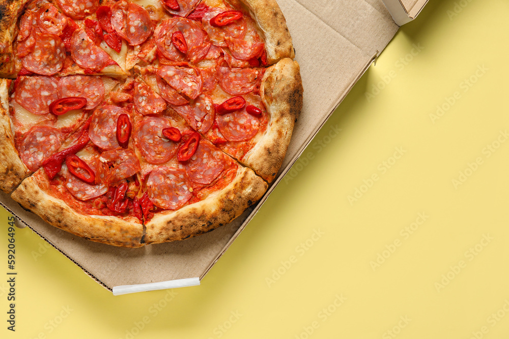 Cardboard box with delicious pepperoni pizza on yellow background