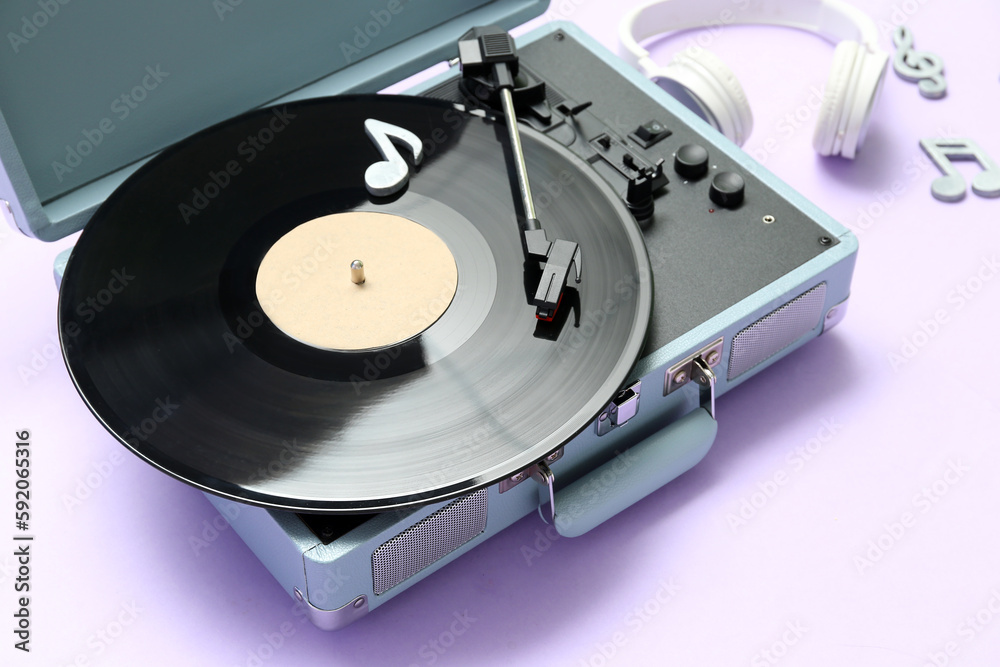 Record player with vinyl disk, headphones and note signs on lilac background, closeup