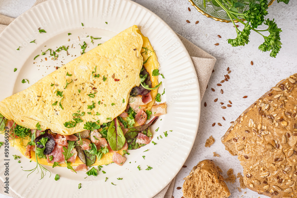 Tasty omelet with ham and greens on light table