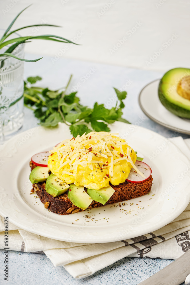 Plate with tasty scrambled eggs sandwich and vegetables on light background