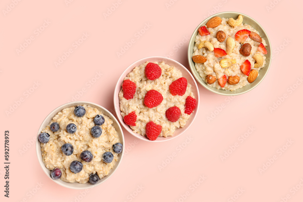 Bowls with tasty oatmeal, blueberries, raspberries and nuts on pink background