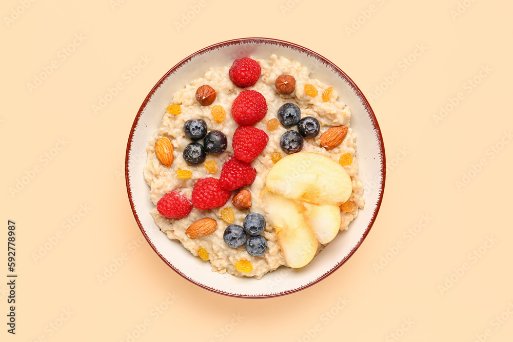 Bowl with tasty oatmeal, ripe berries, nuts, raisins and apple on beige background