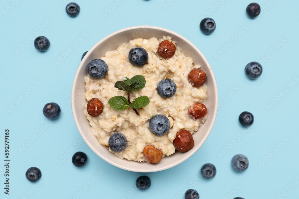 Bowl with tasty oatmeal, hazelnuts and blueberries on blue background