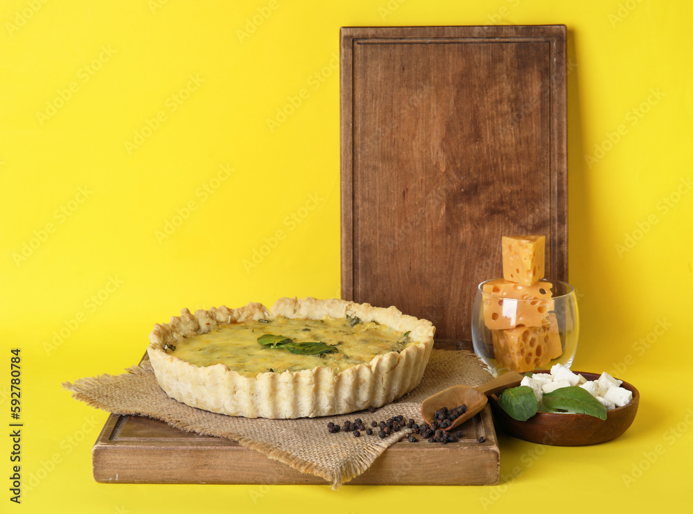 Board with delicious quiche and spinach leaves on yellow background