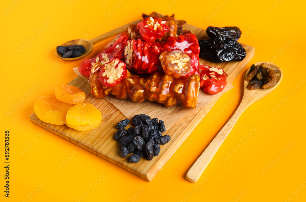 Board with delicious churchkhela and ingredients on orange background